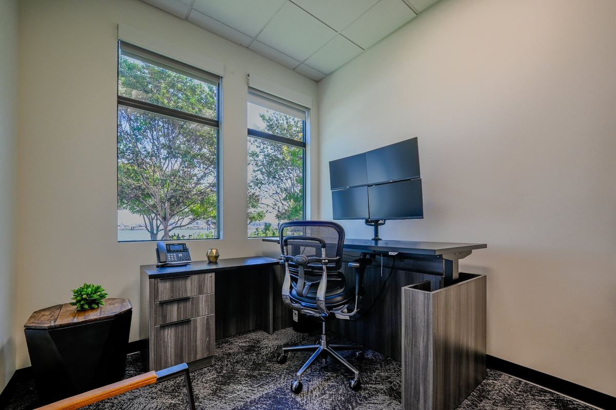 Suite 107: sit-stand executive desk under two tall windows looking toward the water